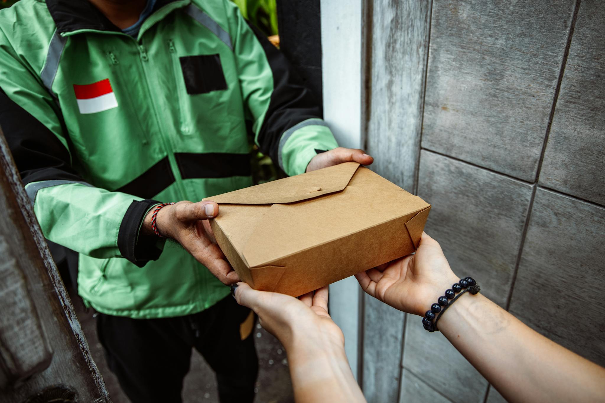 A delivery person hands over a cardboard lunchbox to a customer, showcasing food delivery service.